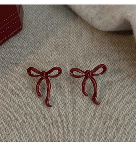 Macro shot of dark red bow earrings on beige knit fabric with a red gift box background