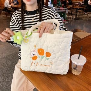 Detail of white quilted canvas tote bag with rabbit embroidery and green flower charm