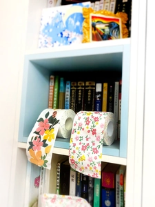 Detail of floral printed toilet paper rolls with pink flowers on a cozy bookshelf