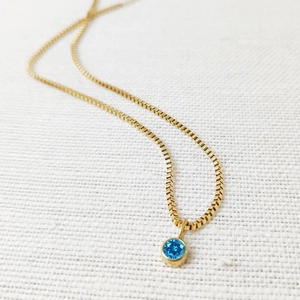 Close-up of a 8mm round blue birthstone pendant on a minimalist gold titanium steel chain
