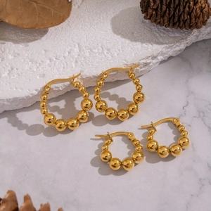 Paire de boucles d'oreilles créoles à billes en acier doré sur fond de marbre