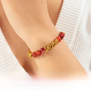 Détail macro des anneaux plaqués or et des perles de résine rouge sur le bracelet