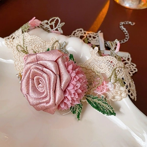Macro detail of floral lace choker with pink fabric roses and pearl accents on ceramic