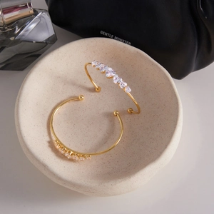 Detail of two gold-plated bangles with heart-shaped cubic zirconia on a ceramic tray