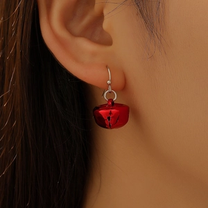 Close-up of a festive red metal bell earring with a silver hook on a female model