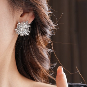 Close-up of silver floral stud earrings with sparkling central zircon on a model