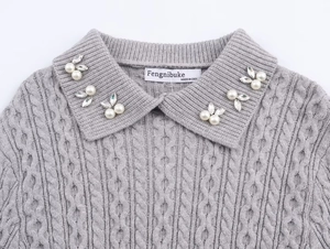 Detalle del cuello de un suéter de punto gris con perlas y motivos de hojas de strass