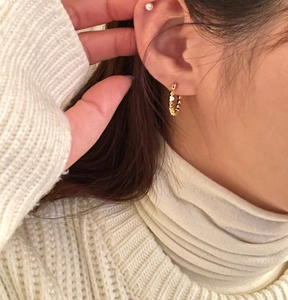 Close-up of heart-textured gold hoop earrings worn on a model with a cozy beige sweater