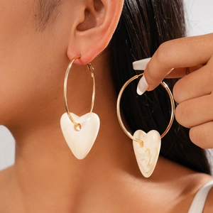 Close-up of golden hoop earring with cream marble acrylic heart pendant on model
