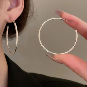 Close-up showing a model wearing large silver geometric C-shaped hoop earrings