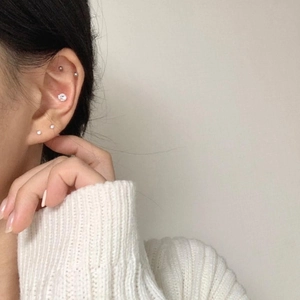 Close-up of minimalist silver zircon earrings worn on multiple ear piercings