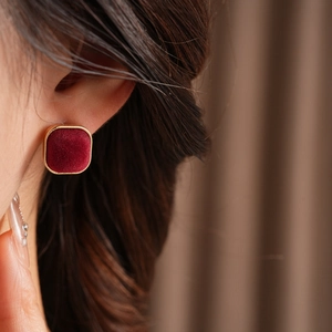 Close-up of red velvet square earrings with gold trim worn by a model in soft light