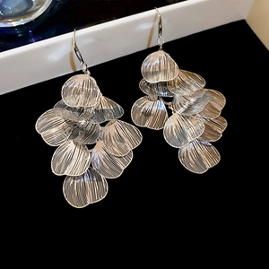 Macro detail of silver hollow petal tassels and layered leaf drop earrings in metal