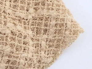 Close-up of beige knitted dress fabric showing intricate lace hollow out mesh texture
