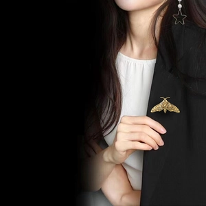 Close-up of a vintage golden moth brooch pinned on a black blazer for styling