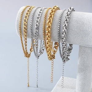 Detailed view of layered gold and silver Cuban chain anklets displayed on a grey stand