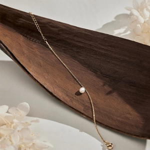 Close-up of minimalist gold chain necklace with a round pearl on textured background