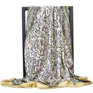 Detailed macro view of pink paisley silk scarf with gold satin edge on a black metal rack