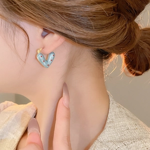 Close-up of heart-shaped light blue enamel earrings with red dots worn on ear