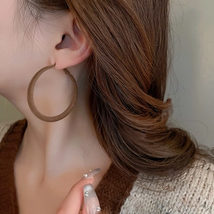Close-up of brown velvet geometric hoop earrings worn by a model in warm light