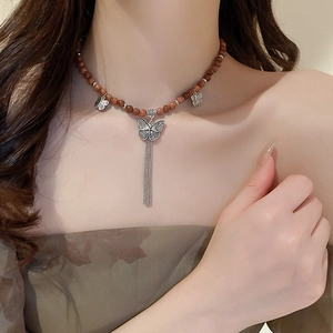 Détail du collier bohème avec perles en bois de santal, papillons argentés et pompons chaîne