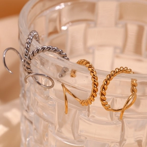 Detailed shot of twisted rope hoop earrings in gold and silver on a glass rim