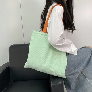 Close-up of green checkered canvas tote bag with vibrant orange shoulder straps
