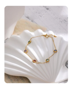 Detail of a thin gold necklace with colorful round stones on a white shell tray