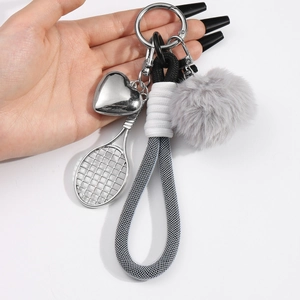 Tennis racket keychain with gray pompom, heart charm, and braided cord on a white background
