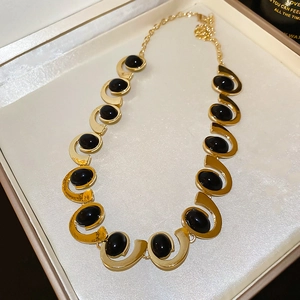 Detailed view of a gold-tone metal necklace with black oval stones in a gift box