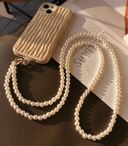 Detail of white pearl phone strap with golden clips on a wavy textured beige case