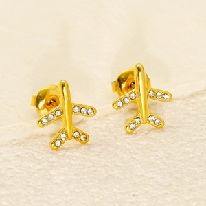 Close-up of golden airplane stud earrings with sparkling crystals on a textured background