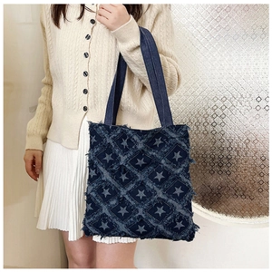 Detail of star pattern and frayed edge denim tote bag on a model in casual knitwear
