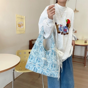 Detailed close-up of a blue canvas shoulder bag with delicate white lace and floral patterns