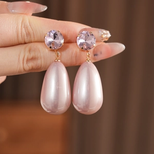 Détail de boucles d'oreilles perles roses en goutte avec cristaux violets en main