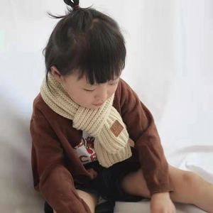 Detailed knit texture of beige children's scarf with a brown leather logo label