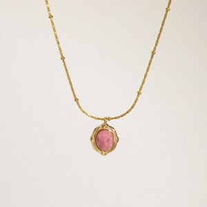 Primer plano detallado del colgante vintage con piedra rosa, relieve dorado y cadena de bolas