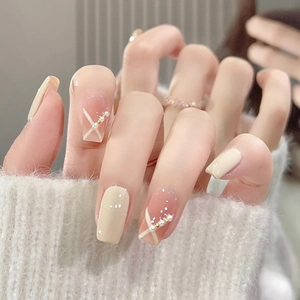 Close-up of nude pink press-on nails with white cross lines, pearls and gold beads