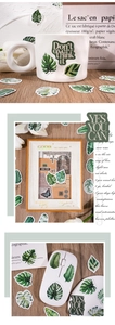 Green leaf stickers decorating a white mug and wooden frame on a natural wood desk
