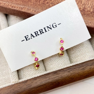Elegant gold earrings with three vertical red zircon stones in a wooden jewelry box