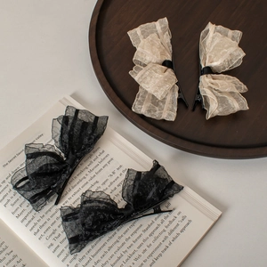Elegant lace bow hair clips in black and beige on a wooden tray with a vintage book