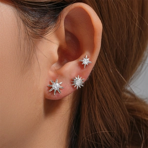 Detailed view of three silver star-shaped stud earrings with zircon stones on the ear