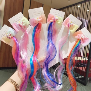 Hand holding colorful unicorn bow hair clips with long curly synthetic hair extensions