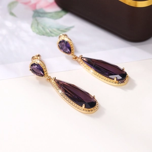Macro shot of gold-plated waterdrop earrings featuring large purple pear-cut zirconia stones