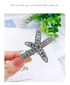 Macro shot of silver starfish hair clip with clear and blue rhinestones held in hand