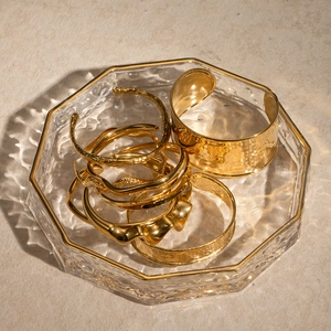 Detailed view of layered 18K gold-plated irregular textured bangles in a glass tray