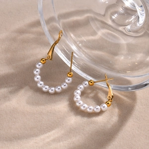 Detailed macro view of gold C-shaped hoop earrings with elegant white pearls on sandy fabric