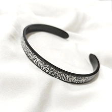 Close-up of black cuff bracelet with intricate silver calligraphy engraving on fabric