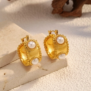 Detail of vintage gold pearl hoop earrings with textured bead edges on a stone background