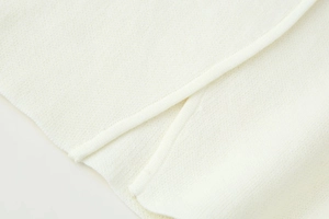 Detail eines weißen Strick-Cardigans mit seitlichem Schlitzsaum und feiner Struktur